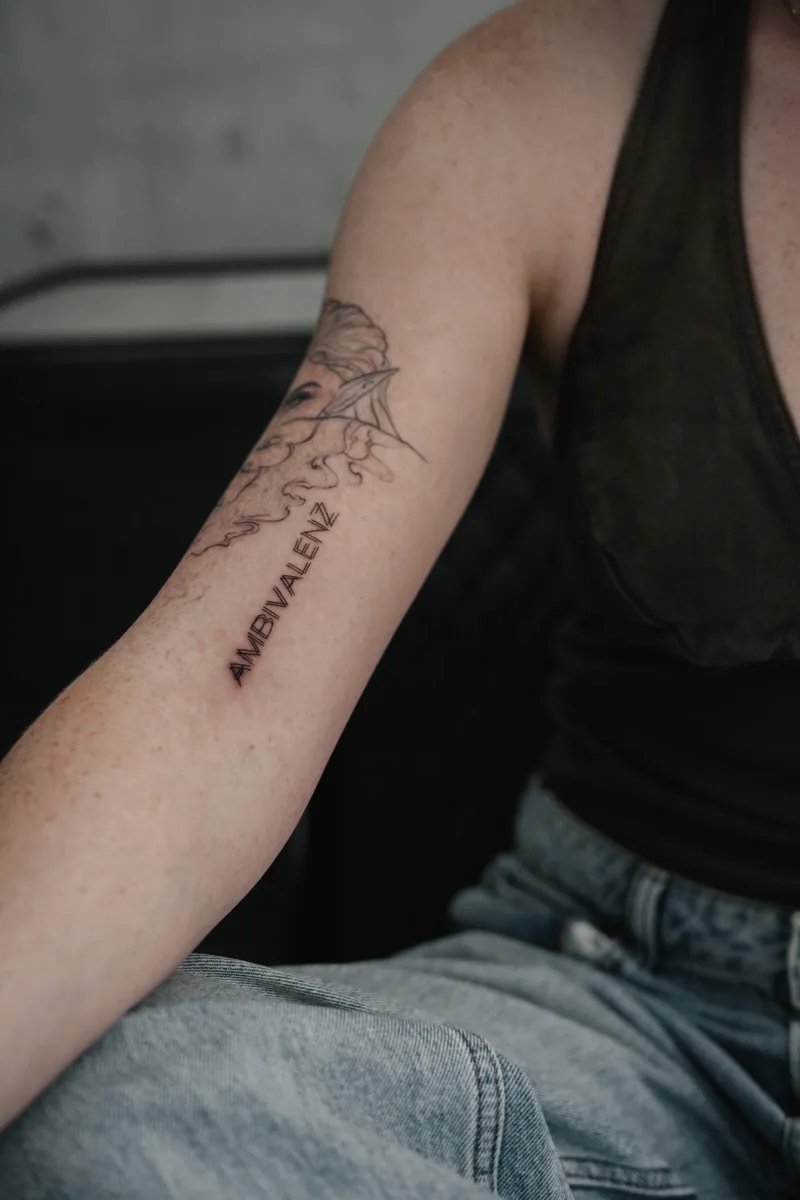 Fine-Line-Schriftzug Ambivalenz am Unterarm